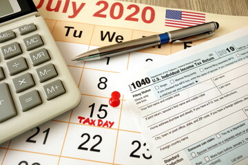 Monthly calendar showing date July 15th 2020 marked as tax day with 1040 form calculator and pen