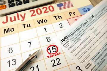 Monthly calendar showing date July 15th 2020 marked as tax day with 1040 form calculator and pen