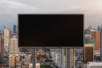 Blank black road billboard with Kuala Lumpur cityscape background at sunset. Street advertising poster, mock up, 3D rendering. Front view. The concept of marketing communication.