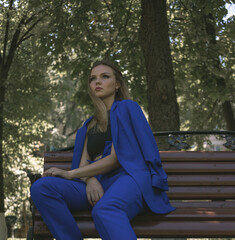 Obraz premium Portrait of a beautiful white girl who sits on a bench. She's wearing an expensive suit and make-up. She sits waiting for someone. High quality photo
