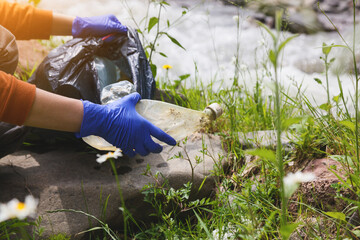 volunteer young woman collecting garbage, picking up plastic bottle waste, land and water...
