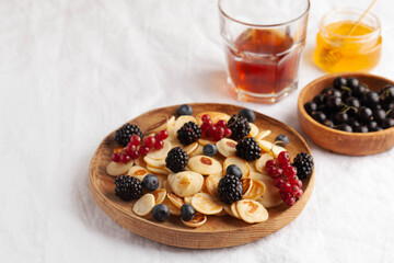 Tiny pancakes with berries and honey on a wooden plate. concept of Breakfast trends in the supply. Copy space