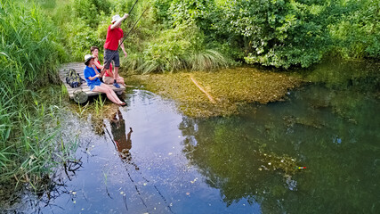 Happy family and friends fishing together outdoors near lake in summer, aerial top view from above
