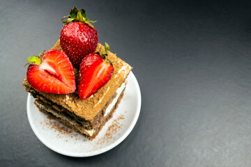 A square piece of tiramisu on a white plate, strawberries.