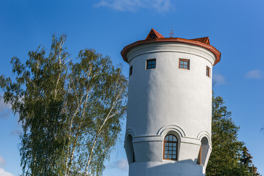 The top of a white tower with a red roof and Windows among trees
