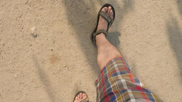 Walking on a sand in sandals and colorful shorts