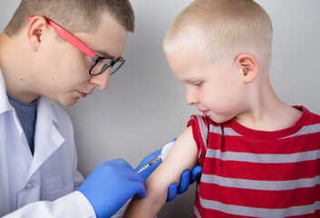 A doctor injects a vaccine into the boy&rsquo;s shoulder. The concept of vaccination of children and the prevention of infectious diseases.