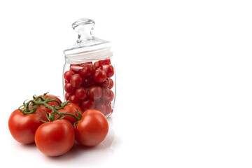 ripe tomatoes on a twig and a glass jar filled with cherries, close-up, white background, horizontal view