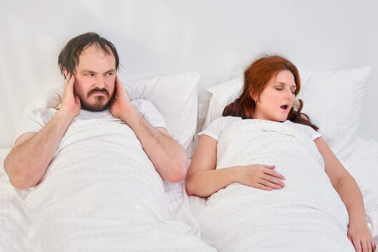 A man puts his hands over his ears because of the noise and snoring of a woman. Sleep problems in family relationships