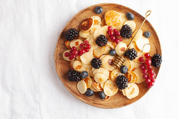 Tiny pancakes with berries in close-up on a white tablecloth. The concept of Breakfast trends in the supply. Copy space