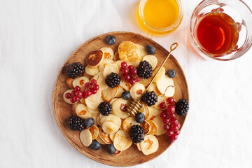 Tiny pancakes with berries, coffee and honey on a wooden plate. concept of Breakfast trends in the supply. Copy space