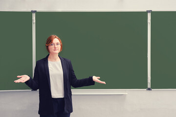 The teacher spreads his hands near the empty school blackboard, copy space for text. Concept of...