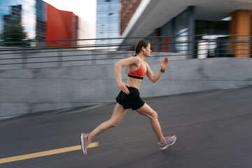 Fototapeta na wymiar Young woman sprinting in the morning outdoors. Side view of female runner in motion working out in the city.