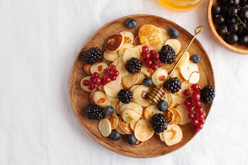 Tiny pancakes with berries and honey on a wooden plate. concept of Breakfast trends in the supply. Copy space