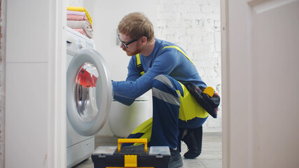Repairman with toolbox near washing machine in bathroom