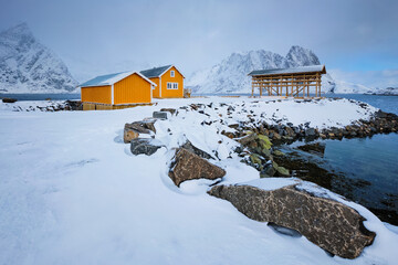Traditional yellow rorbu house in drying flakes for stockfish cod fish in norwegian fjord in winter. Sakrisoy fishing village, Lofoten islands, Norway