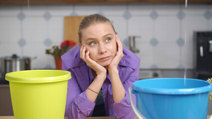 Upset disappointed housewife looking at water dropping from ceiling into plastic buckets in kitchen © nimito