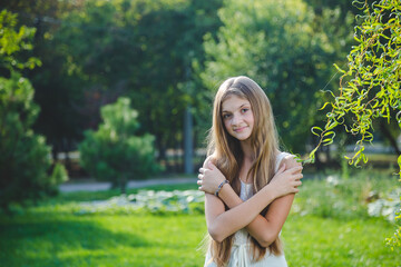 Obraz premium Teenager girl with long hair in white dress in summer park at sunny day