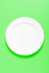 Empty clean round white plate on a green background. Mockup, blank for the designer. Top view, copy space, vertical.