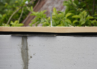 Attaching, installing wood board or plank on gas concrete blocks using masonry concrete screw, concrete fastener with a plastic anchor.