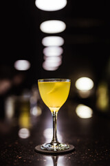 A sour cocktail in a nick and nora glass in a dark and moody atmosphere of a bar