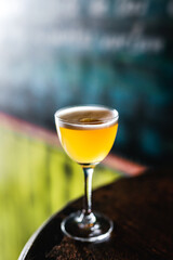 A sour cocktail in a nick and nora glass with orange peel garnish on foam