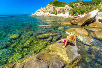 Woman in pink swim suit resting and sunbathing in Cotoncello Beach near popular Sant 'Andrea beach,...