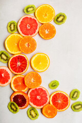 Vertical layout of circles of red orange, tangerines, grapefruit and slices of kiwi on a light gray background.