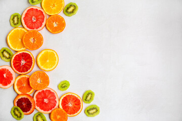 Bright layout of slices of kiwi, slices of red orange, tangerines, grapefruit on a light gray background. Side space for design.