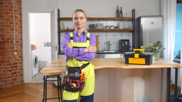 Portrait of female furniture maker in uniform and tool belt smiling at camera