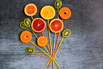 Composition of circles of orange, mandarin, red orange, grapefruit and kiwi in the form of a bouquet on a blue background.