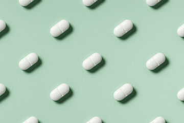medicine, healthcare and pharmacy concept - white pills or capsules lie in rows diagonal on mint green background top view copy space pattern