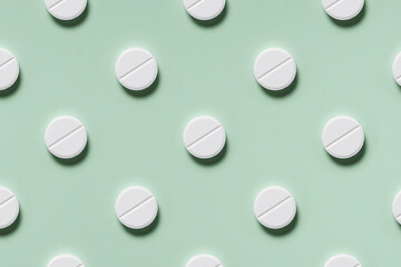 medicine, healthcare and pharmacy concept - white pills or capsules lie in rows diagonal on mint green background top view copy space pattern