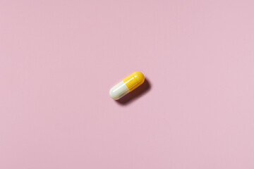 medicine, healthcare and pharmacy concept - white and yellow pill or capsule lies on pink background top view copy space