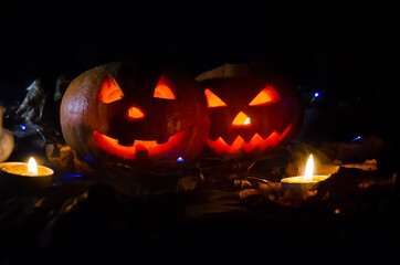 Two glowing pumpkins in the dark in the forest, candles lit around them. Beautiful background for Halloween.