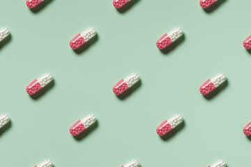 medicine, healthcare and pharmacy concept - white and pink pills or capsules lie in rows diagonal on mint green background top view copy space pattern
