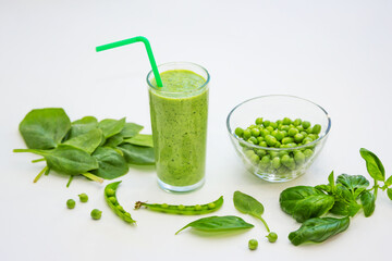 Smoothie in a glass and ingredients – green peas, basil and spinach leaves on a white background. Healthy vegan cocktail. 