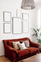 Blank picture frames mockups on white wall. White living room design. View of modern boho, scandi style interior with sofa, cushions, potted palm plant. Home staging concept, decorating. Vertical.