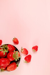 Bowl with fresh strawberries on pink background. Summer composition, vertical photo
