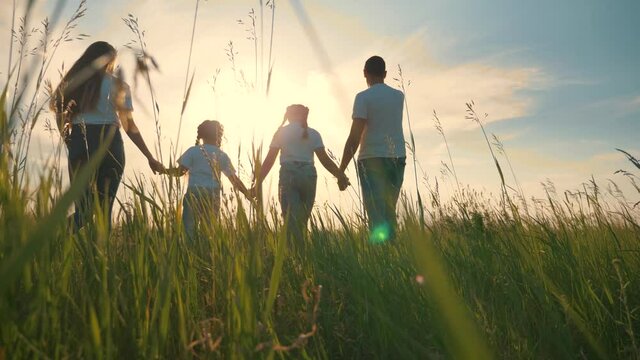 Happy family together. People hold hands on a walk on the green grass. The concept of teamwork. Happy father with daughters.