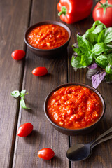 Balkan sauce ajvar in a clay bowl and ingredients for its preparation on a wooden background. Serbian traditional food