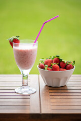 Strawberry smoothie and a bowl of strawberries on a wooden table in the garden