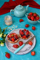 Appetizing cake with strawberries, fresh ripe strawberries in a bowl and a teapot on a turquoise table. Vertical. The concept of a summer dessert.