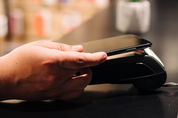 Costumer pays phone nfc terminal in the shop. Close up. Men take phone in the hand and pays in terminal. 