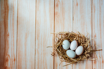 White eggs in hay nest on wooden table background, top view with free space