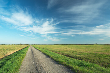 Gravel road on flat terrain and white clouds on blue sky