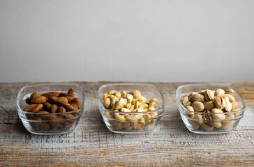 Almond, pistachio and cashew in a small plates which standing on a vintage white table. Nuts is a healthy vegetarian protein and nutritious food.