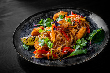 Tasty asian noodles with fried cheese tofu and vegetables in plate on black wooden table background