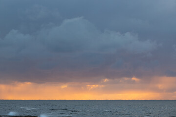 Sea horizon view with orange sunlight and cloudy sky.