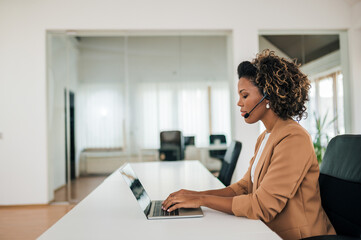 Side view portrait of a beautiful young businesswoman working with laptop and headset.